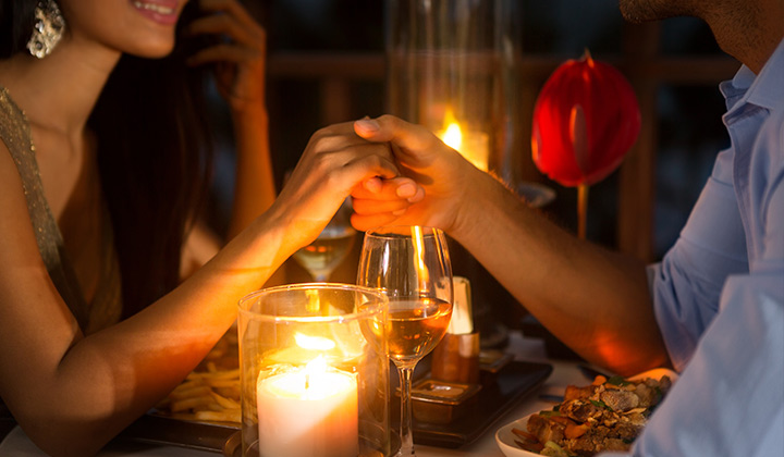 Romantic couple holding hands together over candlelight during romantic dinner 