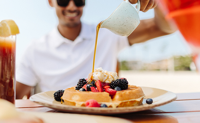 Guest pouring syrup on their waffles with berries and whip cream on their 3-day foodie itinerary in San Diego at The Grill at Torrey Pines Oceana Coastal Kitchen
