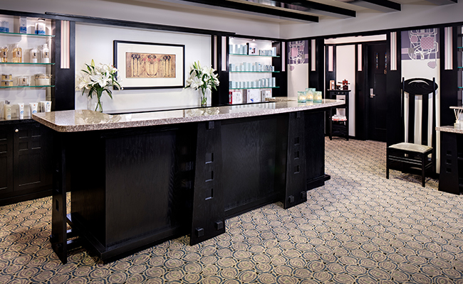 The reception area of The Spa at Torrey Pines is designed in the style of Scotsman Charles Rennie Mackintosh featuring dark wood reception desk, patterned carpet, and a famous high-back chair.