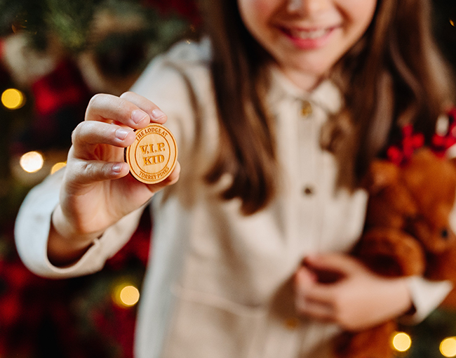 Young girl holding up a VIP wooden Coin at The Lodge at Torrey Pines