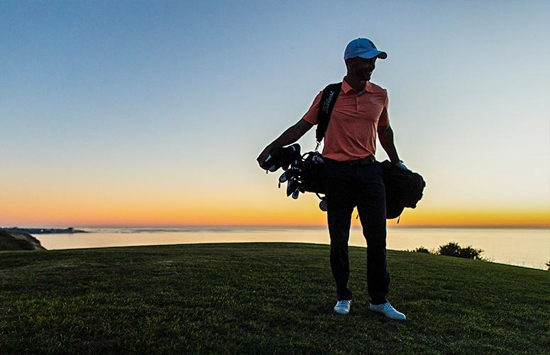 Golfer carrying golf bag and clubs on the Torey Pines golf course at dusk